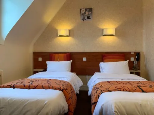 Chambre à deux lits jumeaux avec couvre-lits orange à motifs floraux et appliques murales allumées