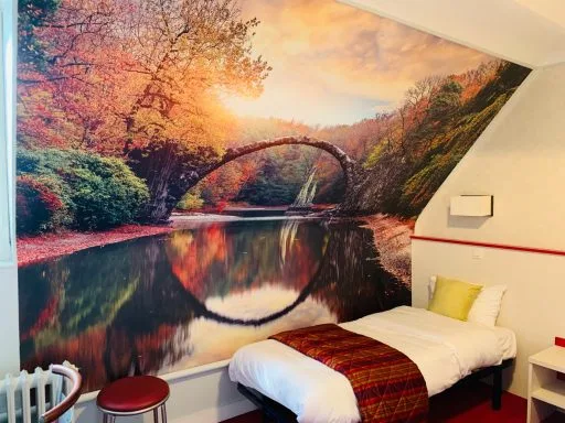Chambre avec fresque murale représentant un pont enjambant une rivière automnale, couvre-lit à carreaux rouges