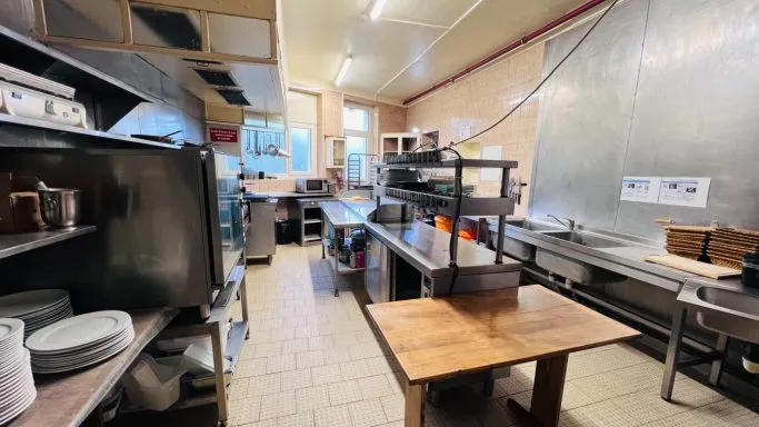 Cuisine professionnelle avec plans de travail inox, piles d'assiettes blanches et desserte en bois centrale