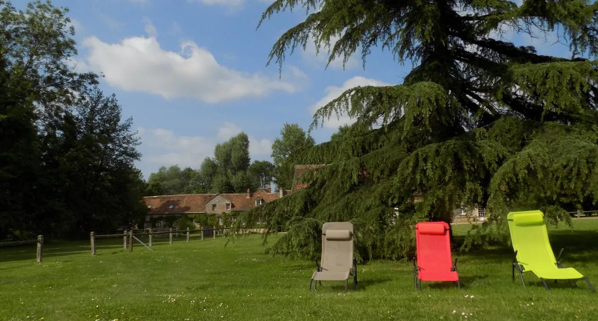 Gîte de groupe Gîtes du Moulin de Sainte Croix à Neuillé-le-Lierre — Vue extérieure des gîtes du Moulin de Sainte Croix avec jardin arboré et rivière Brenne, capacité 30 personnes