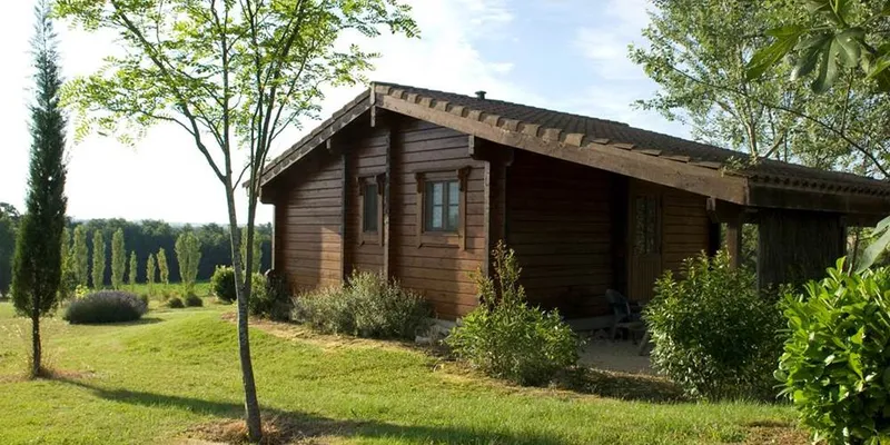 Façade d'un chalet en bois avec entrée ombragée sous les arbres du domaine