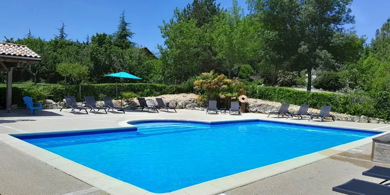 Piscine de douze mètres sur six entourée de transats et de pelouse verte