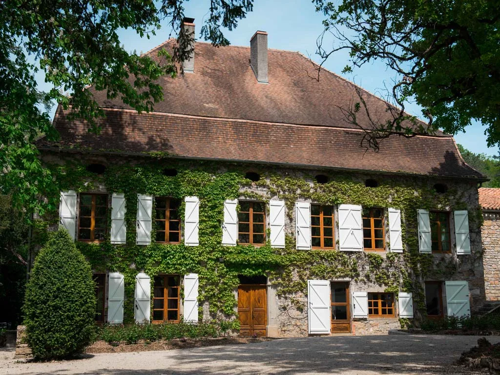 Gîte de groupe Gîte La Rivière à Calvignac — Façade en pierre du Gîte La Rivière à Calvignac avec parc arboré en arrière-plan, capacité 15 personnes