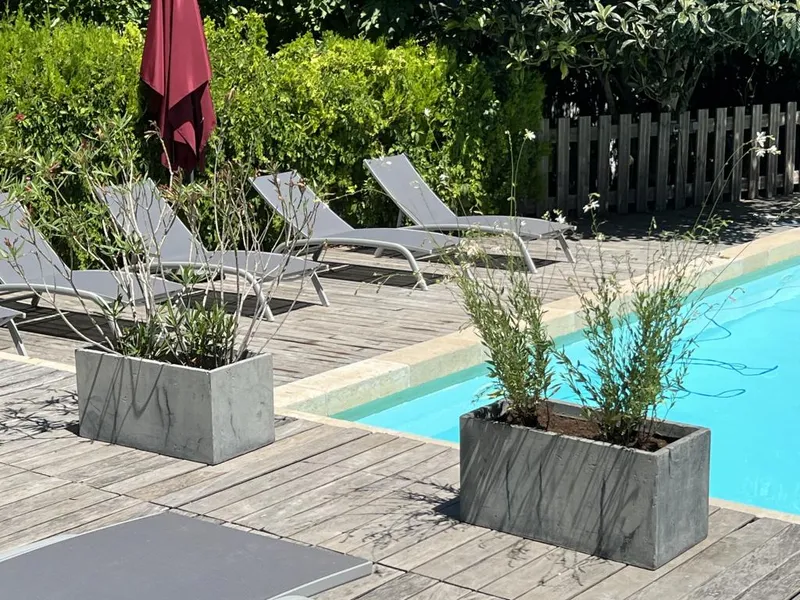 Terrasse en bois autour de la piscine avec transats parasol et jardieres fleuries