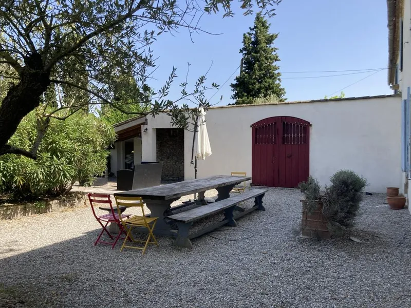 Coin repas exterieur avec grande table en bois sous un olivier et portes de grange rouges