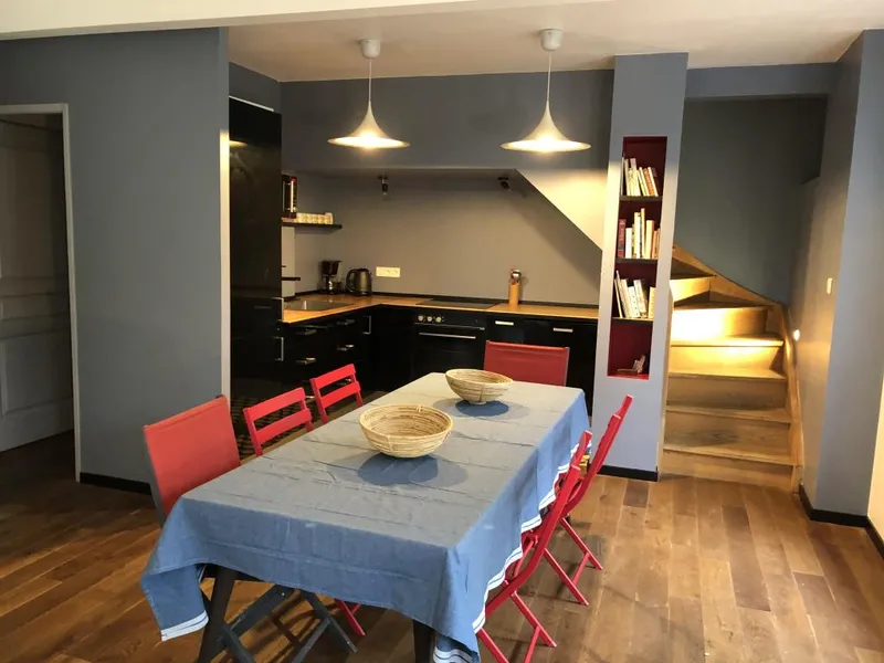 Cuisine equipee noire avec coin repas chaises rouges et escalier en bois eclaire