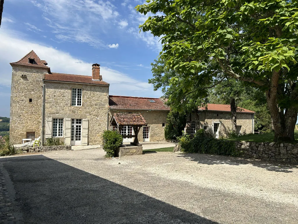 Gîte de groupe Le Domaine de Las Bouzigues à Clermont-Dessous — Cour en gravier avec bâtiment principal en pierre de taille sous ciel bleu, capacité 57 personnes